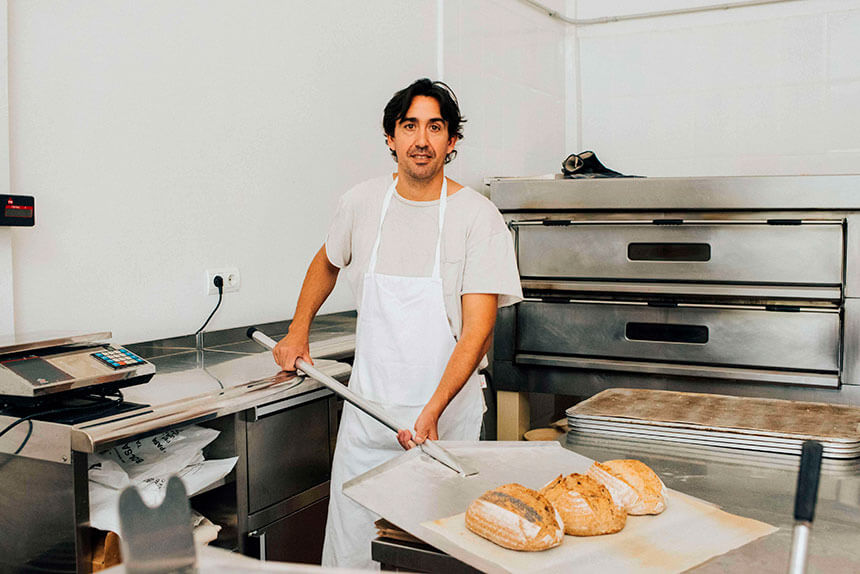 Plano Americano de Pedro Puche, que lleva delantal y sujeta una pala de metal para extraer el pan. Al fondo vemos los compartimentos del horno.